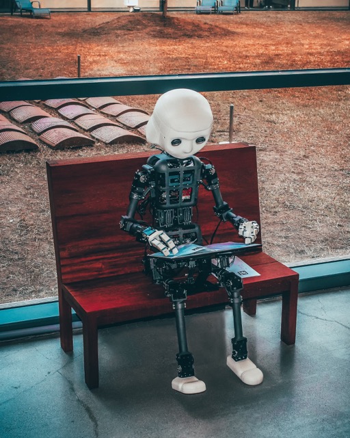 Ein humanoider Roboter sitzt auf einer Bank und bedient ein Tablet